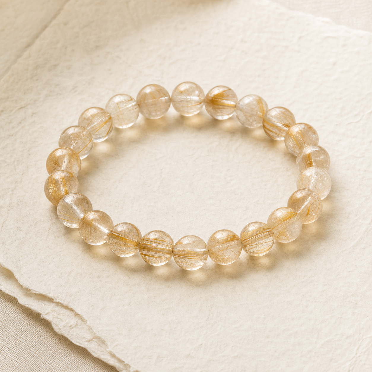 Natural rutilated quartz gemstone bracelet with golden inclusions on warm ivory paper